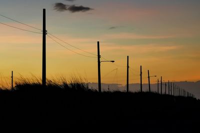 Silhouette electricity pylons on land against sky during sunset