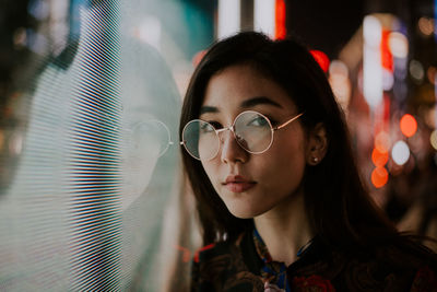 Portrait of young woman standing against illuminated city at night