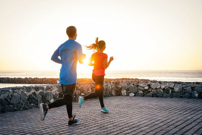 Couple jogging on promenade against clear sky during sunset