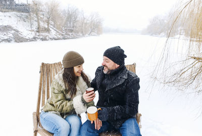 Side view of smiling friends sitting on snow