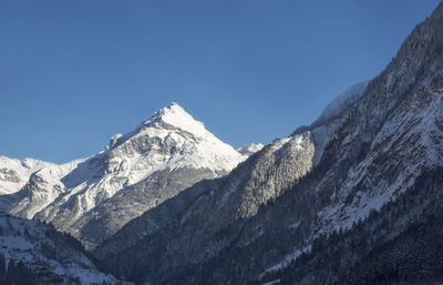 Low angle view of snowcapped mountains against clear blue sky