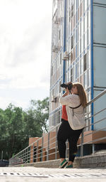 Rear view of women holding camera walking on footpath in city