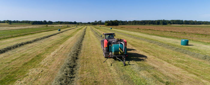 Black tractor with a red straw chamber press during the straw harvest on a mown field