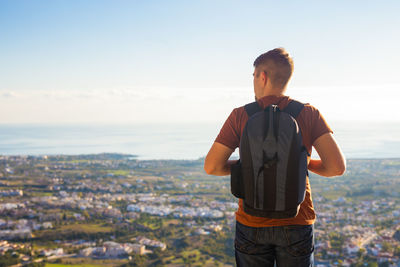 Rear view of man looking at cityscape against sky