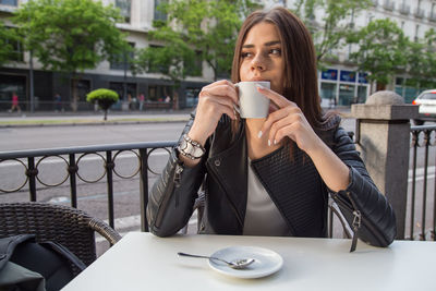 Young woman having coffee looking away while sitting at sidewalk cafe
