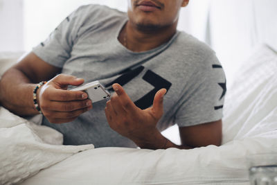 Midsection of man checking blood sugar level on glaucometer while lying on bed at home