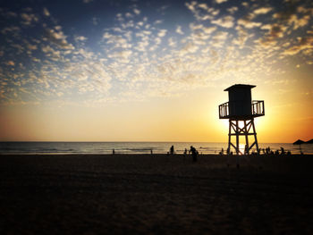 Silhouette lifeguard hut on beach against sky during sunset