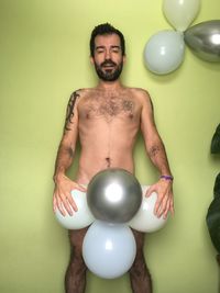 Portrait of young man with balloons standing against wall