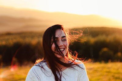 Close-up of woman smiling on field against sky during sunset