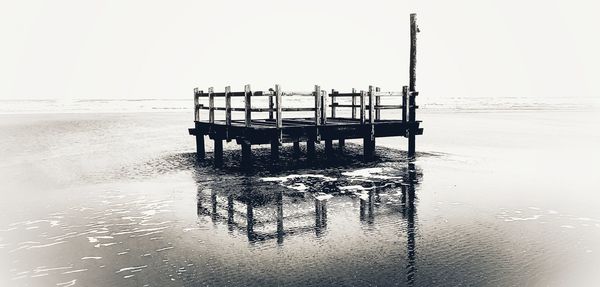 Wooden posts on pier over sea against clear sky