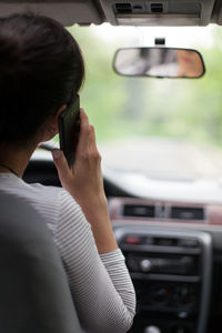 Rear view of woman using mobile phone in car
