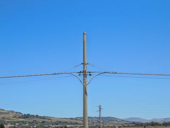 Low angle view of electricity pylon against clear blue sky