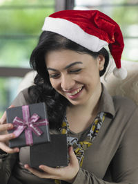 Happy young woman opening christmas gift at home