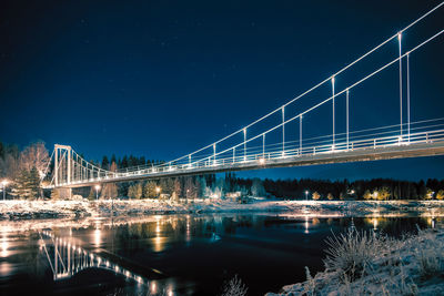 Illuminated bridge over river against sky at night