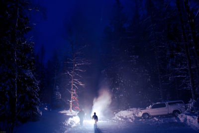 Men walking on snow by illuminated car at night