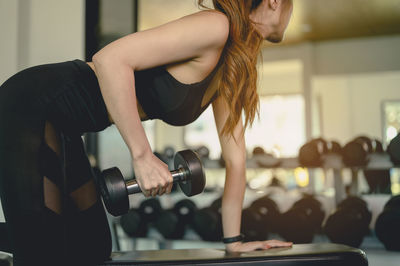 Midsection of woman exercising with dumbbell at gym