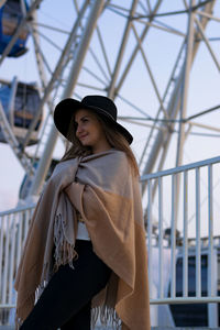 Young woman wrapped in blanket looking away while standing at amusement park