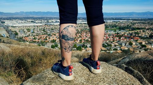 Low section of woman with tattoo standing on mountain against sky