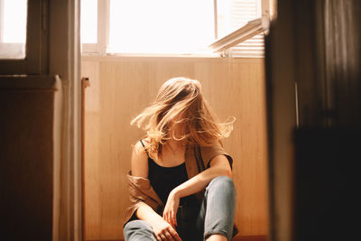 Young woman tossing hair while sitting on floor in balcony in summer