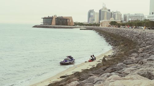 People on sea by city against clear sky