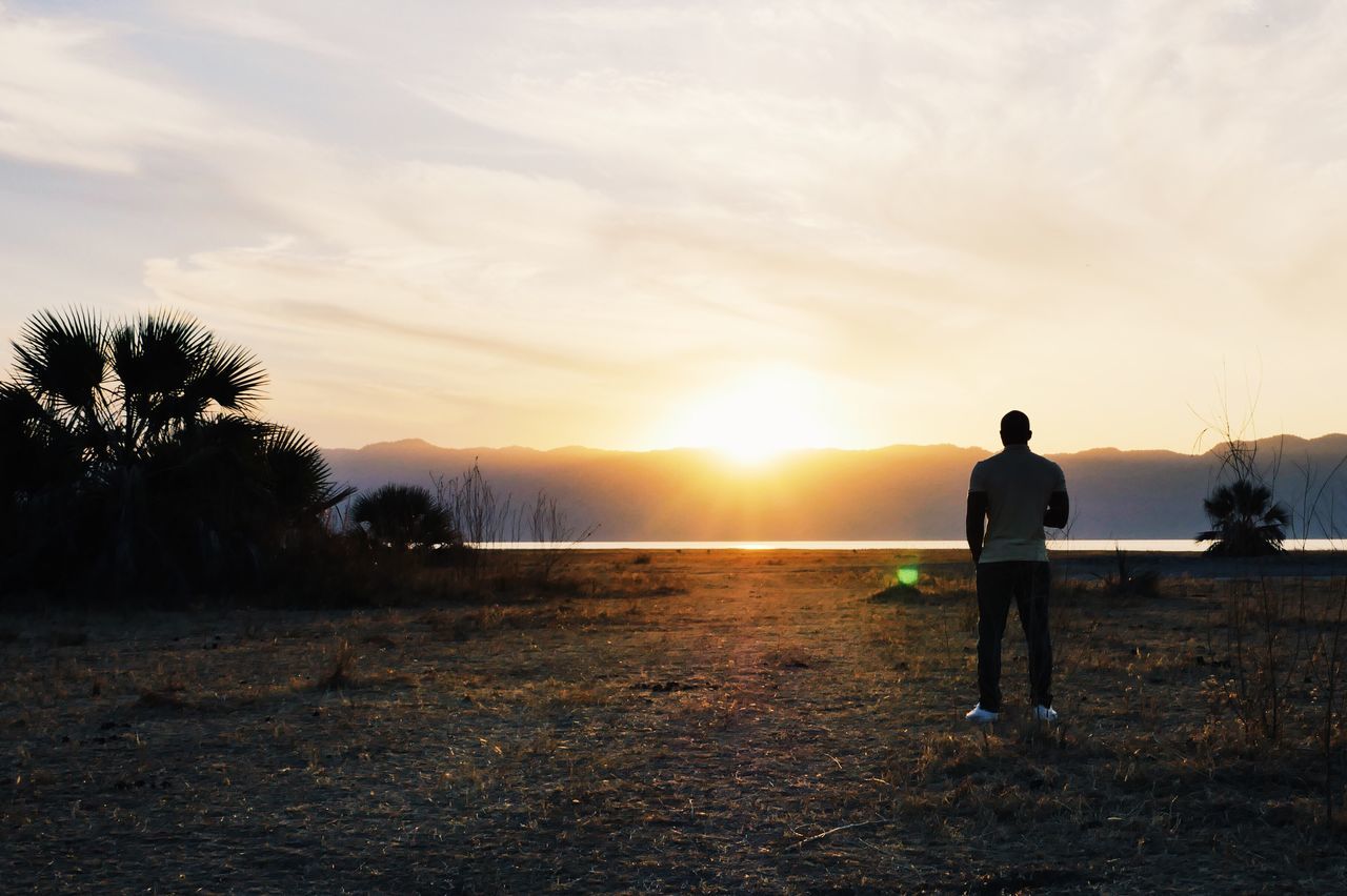 sunset, full length, standing, rear view, tranquil scene, scenics, sky, beauty in nature, tranquility, sun, casual clothing, nature, mountain, cloud - sky, outdoors, vacations, non-urban scene, remote, mountain range