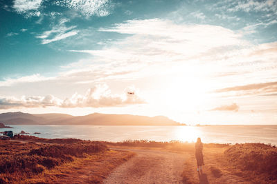 Rear view of woman standing by sea against sky during sunset