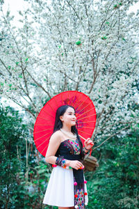 Young woman with umbrella standing against trees