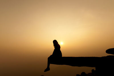 Silhouette woman sitting on rock against sky during sunset