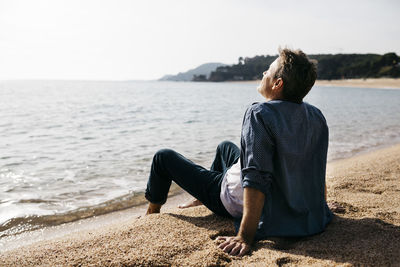 Relaxed man sitting on shore at beach during sunny day