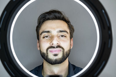 Handsome man seen through illuminated ring light against gray wall