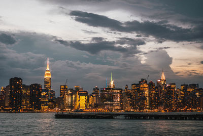 Illuminated buildings in city against cloudy sky