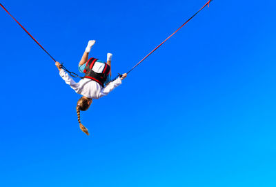 Rear view of girl bungee jumping against clear blue sky