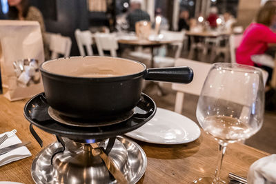 Heated pot of swiss cheese fondue alongside wineglass on dining table