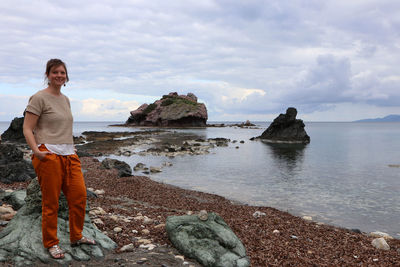 Portrait of woman standing on rock at sea shore against sky