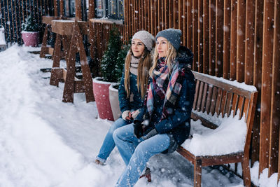 Two women on a winter snowy day sit on a bench and enjoy the weather.