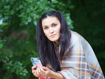 Portrait of woman holding mobile phone outdoors