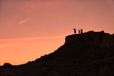 Silhouette people standing on cliff against sky during sunset