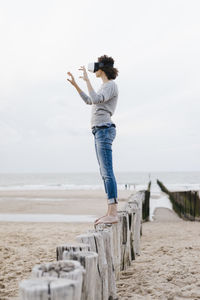 Woman standing on wooden stake on the beach wearing vr glasses