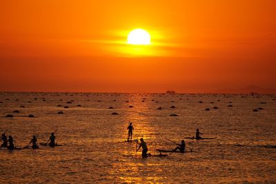 Silhouette people in sea against orange sky