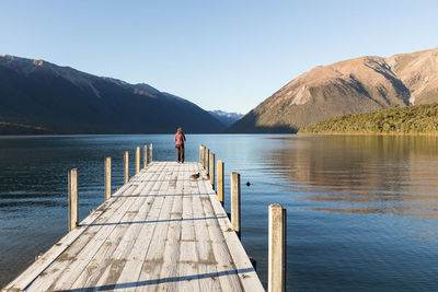 Rear view of woman standing pier over lake against sky