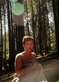 Portrait of shirtless woman covered in blanket at forest