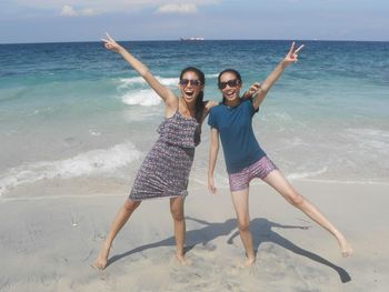 Full length portrait of smiling siblings gesturing while standing at beach