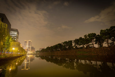 Scenic view of lake by buildings against sky at night