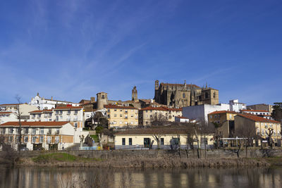 Buildings by river against blue sky