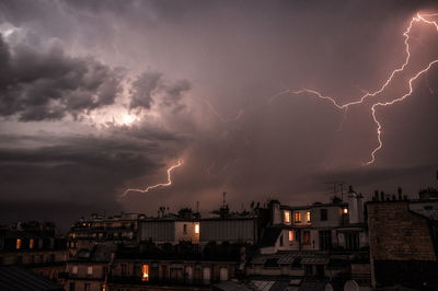 Buildings in city against thunderstorm at night