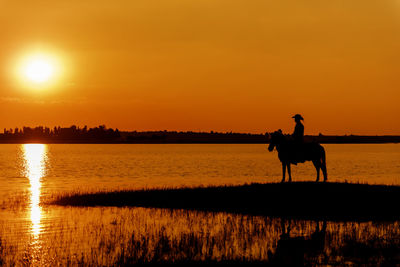 Silhouette people riding horse on lake during sunset