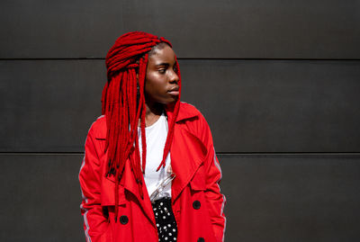 Portrait of young woman standing against red wall