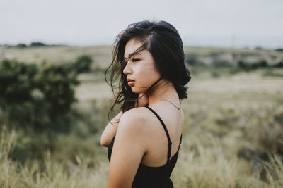 Young woman looking away while standing on field against sky