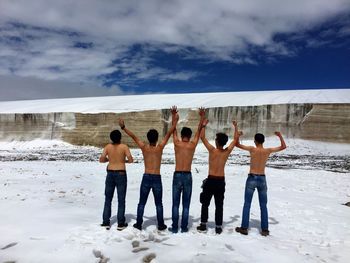 Rear view of shirtless friends on snow covered field with arms raised