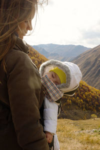 Portrait of woman with her little daughter in ergo carrier on a background of autumn mountains.